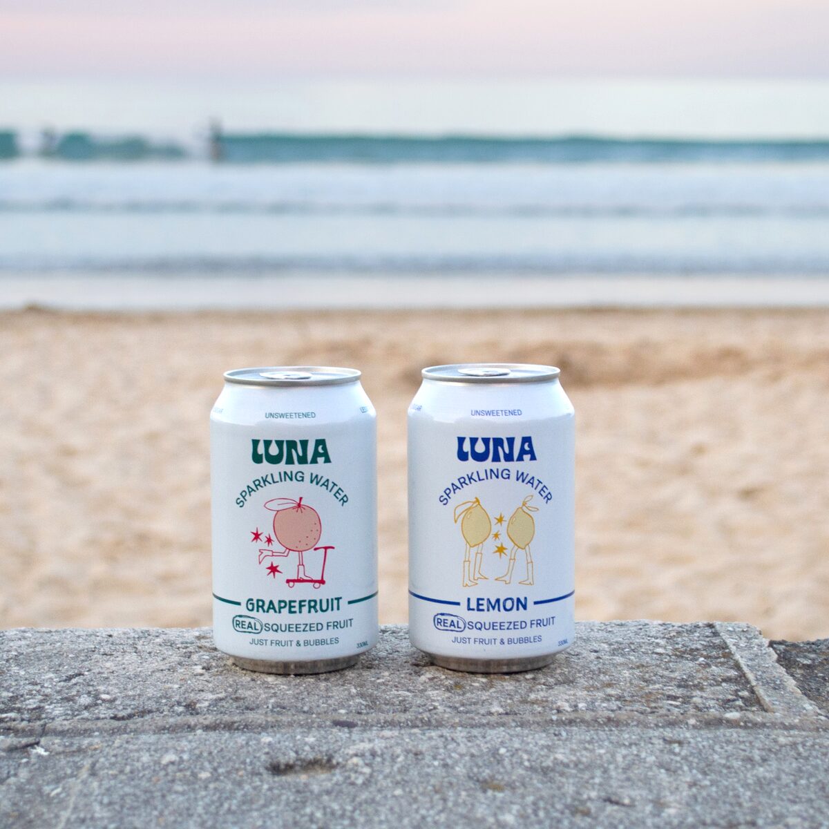 Luna Grapefruit and Lemon cans side by side on a seawall at the beach