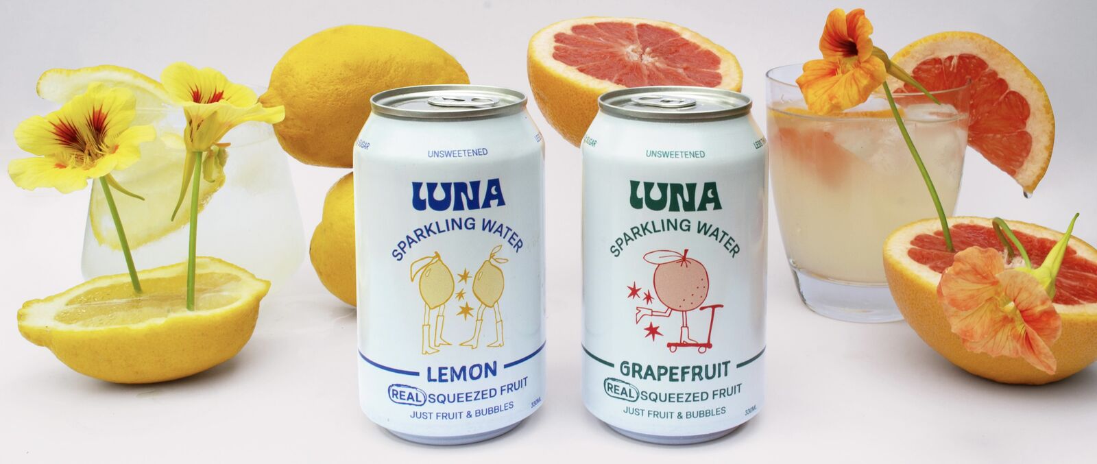 Luna Lemon and Grapefruit sparkling water cans with fresh lemons, grapefruit and nasturtium flowers
